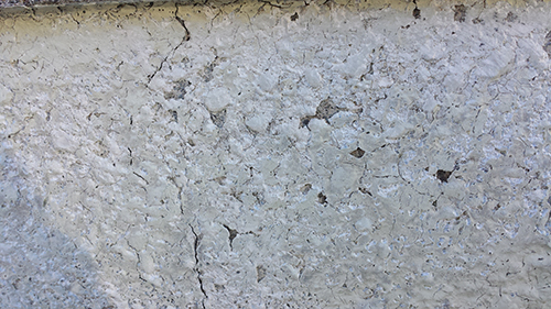 Cracked concrete wall with a rough, light gray surface and visible fissures