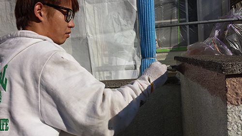 Worker in a white hoodie applying plaster to a concrete wall with a trowel, wearing gloves and safety glasses in a construction setting