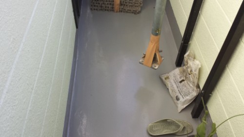 Narrow hallway with a wet floor, a broom leaning against the wall, a slipper, and a crumpled newspaper.
