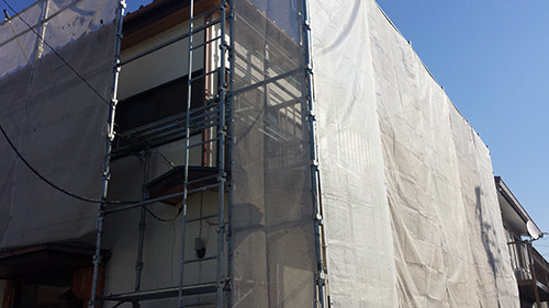 Scaffolding around a building covered with white construction tarp on a sunny day