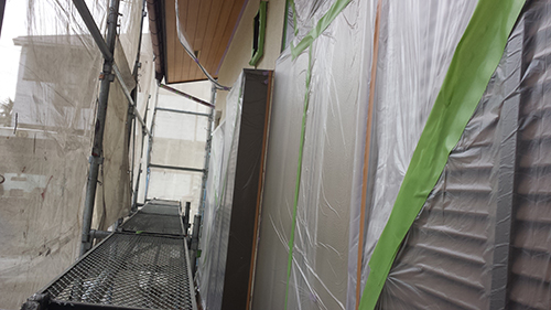 Narrow construction corridor with scaffolding, metal walkway planks, and plastic sheeting walls taped for protection.