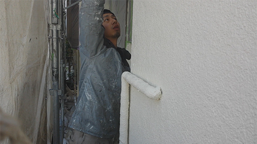 Painter applying white paint to a wall with a roller on scaffolding between buildings
