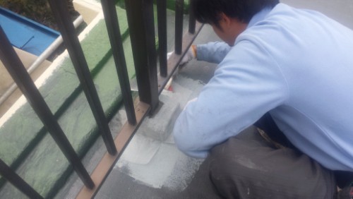 koushin_20140319-1058141 | 外壁塗装は神奈川県横浜市の塗装職人 Worker on a rooftop applying sealant along the edge beside a metal railing.