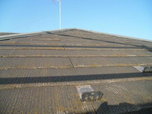 koushin_CIMG1144-1 | 外壁塗装は神奈川県横浜市の塗装職人 Close-up view of a sloped roof with dark, mossy shingles, a peak in the distance, and a clear blue sky.