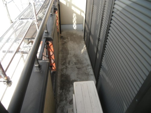 koushin_CIMG1145-1 | 外壁塗装は神奈川県横浜市の塗装職人 Narrow outdoor balcony walkway between a building with metal shutters on the right and a metal railing on the left, with a white plastic step on the floor.