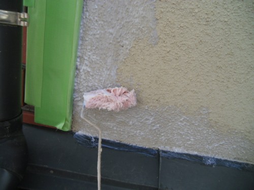 koushin_CIMG1201-1 | 外壁塗装は神奈川県横浜市の塗装職人 Paint roller applying beige plaster to an exterior wall near green protective tape and a black baseboard.