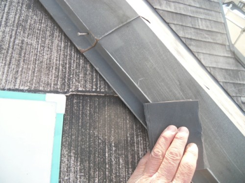 koushin_CIMG1204-1 | 外壁塗装は神奈川県横浜市の塗装職人 Hand pressing a dark square patch onto a sloped roof beside metal flashing during repair work