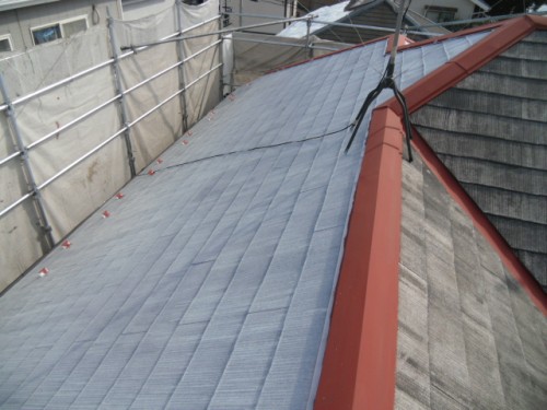 koushin_CIMG1211-1 | 外壁塗装は神奈川県横浜市の塗装職人 Metal roof being repaired with scaffolding and safety rope along a red ridge cap.