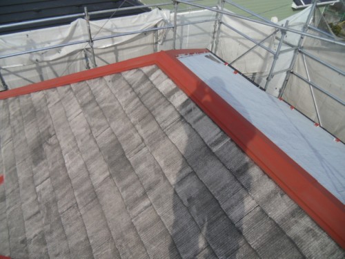 koushin_CIMG1213-1 | 外壁塗装は神奈川県横浜市の塗装職人 Sloped roof under renovation with gray tiles, red metal flashing along the edge, and scaffolding in the background.