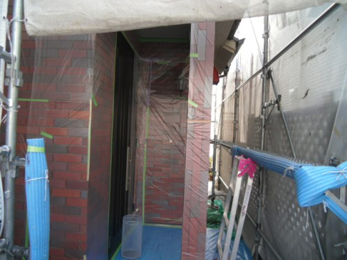 koushin_CIMG1220-1 | 外壁塗装は神奈川県横浜市の塗装職人 Construction site entry with brick walls, scaffolding on both sides, and blue protective coverings taped along the doorway.