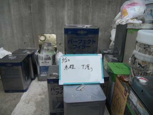 koushin_CIMG1224-1 | 外壁塗装は神奈川県横浜市の塗装職人 Outdoor storage area with various paint cans and containers; a whiteboard-style note reads '外壁 下塗り' (exterior wall undercoat).