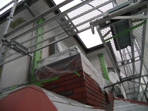 koushin_CIMG1227-1 | 外壁塗装は神奈川県横浜市の塗装職人 Scaffolding surrounds a brick chimney on a building; brickwork is covered with plastic sheeting and taped edges.