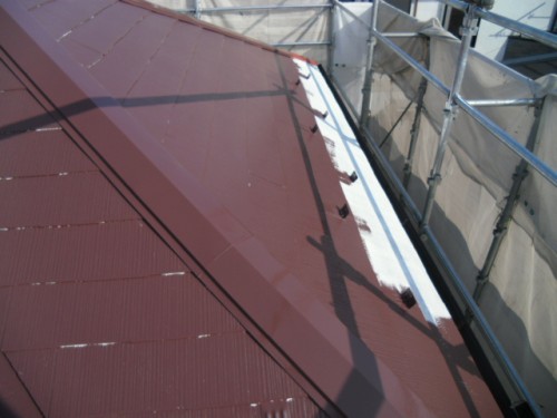 koushin_CIMG1230-1 | 外壁塗装は神奈川県横浜市の塗装職人 Close-up of a reddish metal roof with a white sealant along a ridge, surrounded by scaffolding during construction.