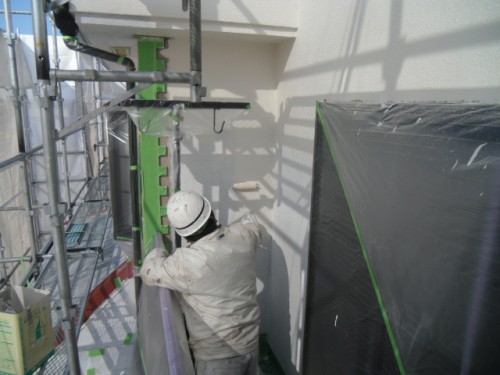 koushin_CIMG1232-1 | 外壁塗装は神奈川県横浜市の塗装職人 Construction worker in a hard hat on scaffolding fastening a green metal bracket to an exterior wall