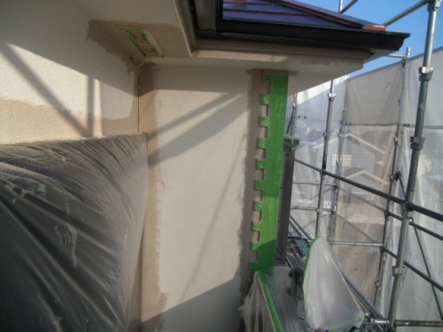 koushin_CIMG1234-1 | 外壁塗装は神奈川県横浜市の塗装職人 Close-up of a green metal mounting rail attached to a beige exterior wall, with scaffolding visible on the right during construction.