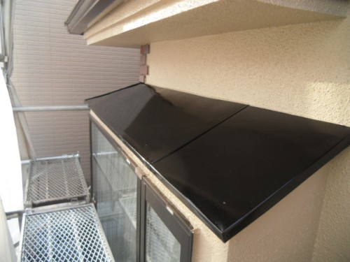 koushin_CIMG1262-1 | 外壁塗装は神奈川県横浜市の塗装職人 Black, angled awning over a beige stucco window, with scaffolding visible on the left side of the exterior wall.