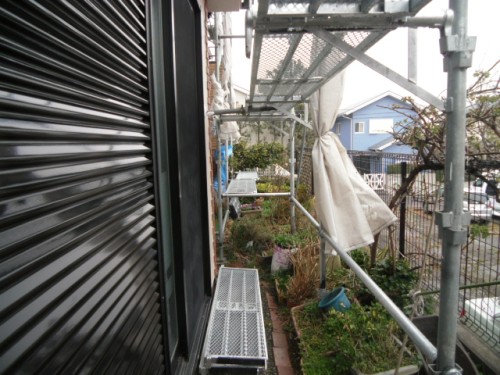 koushin_CIMG1267-1 | 外壁塗装は神奈川県横浜市の塗装職人 Exterior view of scaffolding erected beside a house, with a metal walkway and black shutter on the left.