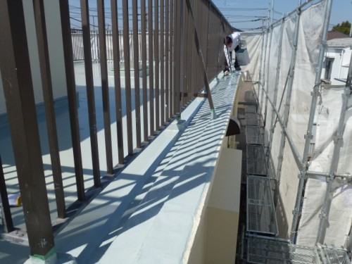 koushin_P10208241 | 外壁塗装は神奈川県横浜市の塗装職人 Construction worker on a narrow elevated ledge with metal railing and scaffolding along a building site.