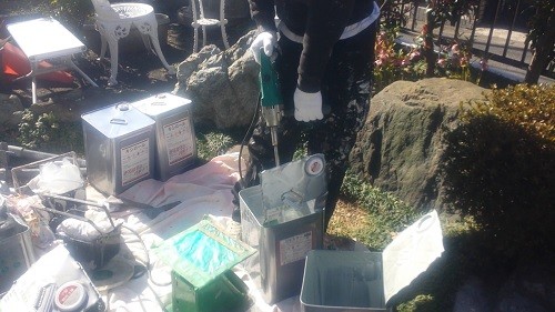 koushin_kakuhan1 | 外壁塗装は神奈川県横浜市の塗装職人 Person in gloves operating a tool at an outdoor workshop with metal jugs and containers on a tarp.