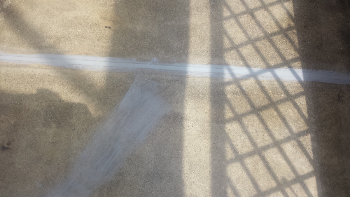 METADATA-START | 外壁塗装は神奈川県横浜市の塗装職人 Sunlit concrete ground showing a white stripe with shadows from a railing casting a grid pattern across the surface.