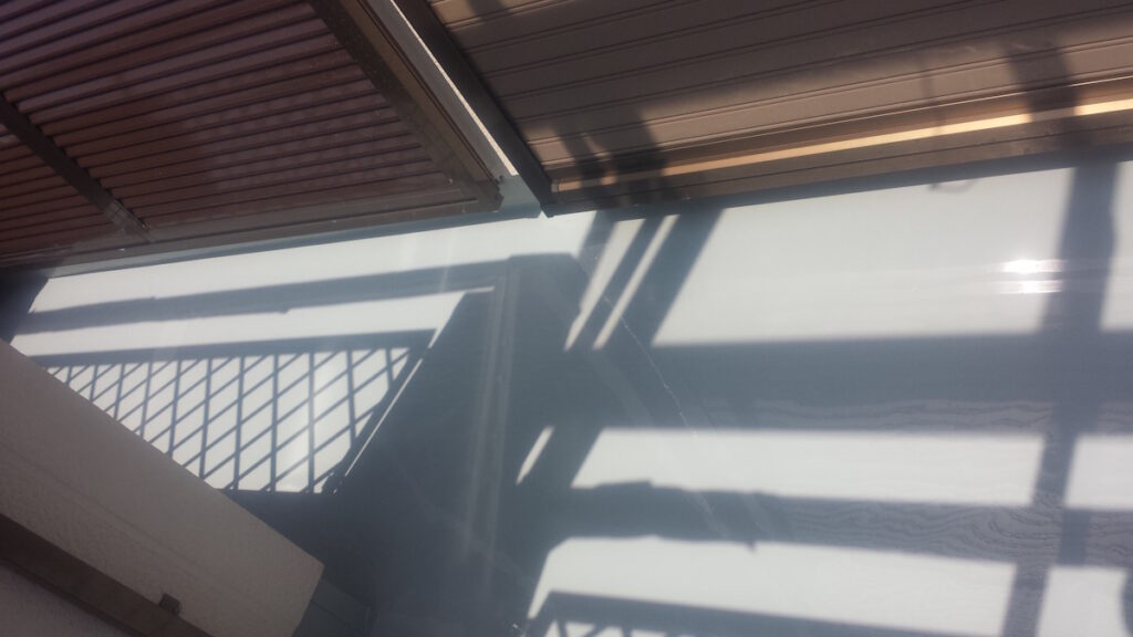 Sunlight casts angular shadows of a railing and window blinds across a pale floor surface in a bright indoor space.