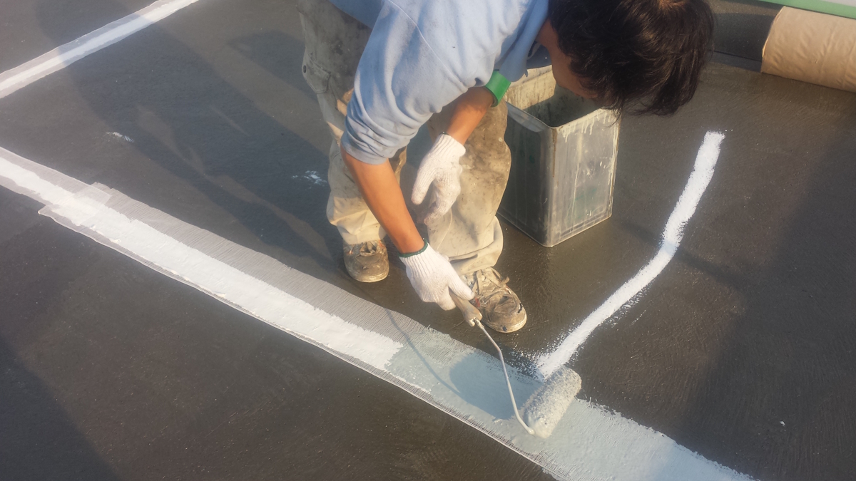 METADATA-START | 外壁塗装は神奈川県横浜市の塗装職人 Worker in gloves rolling white paint along a line on a flat rooftop.