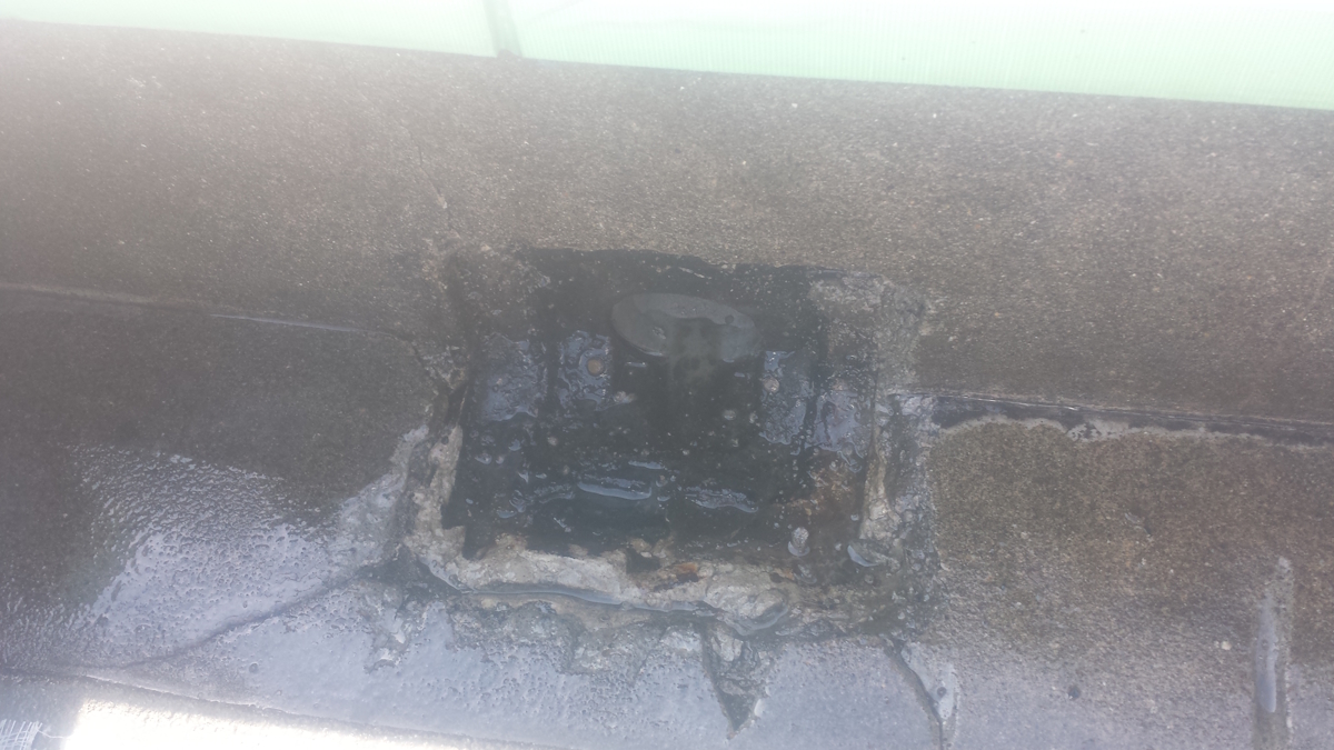 METADATA-START | 外壁塗装は神奈川県横浜市の塗装職人 Close-up of a deteriorated roof area with a square hole filled with dark tar and wet around it, indicating water damage.