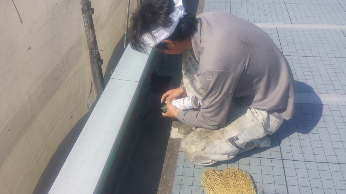 METADATA-START | 外壁塗装は神奈川県横浜市の塗装職人 Worker kneels on a tiled rooftop edge, applying sealant with a caulking tube beside a broom.