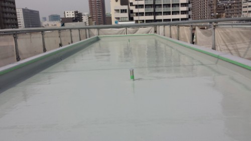 20140416-083711-1 | 外壁塗装は神奈川県横浜市の塗装職人 Rooftop with a shallow, reflective waterproof surface and green edge trim; city buildings visible in the background.