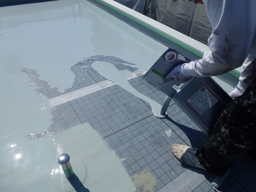 P1030205 | 外壁塗装は神奈川県横浜市の塗装職人 Worker in gloves applies a light gray waterproof coating with a caulking gun on a grid-patterned roof surface edge.