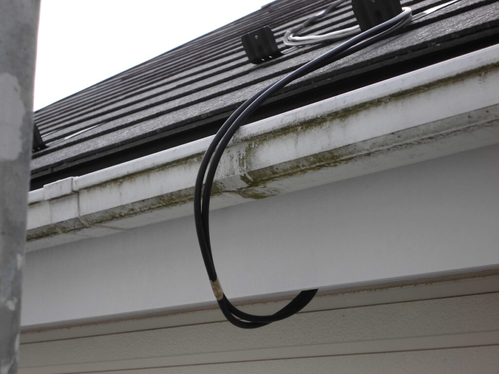 A black cable loop hanging from the edge of a roof gutter with moss along the fascia.
