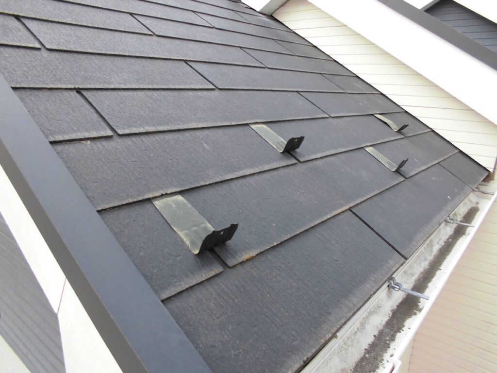 Close-up of a dark shingled roof with three metal mounting brackets attached to the tiles.
