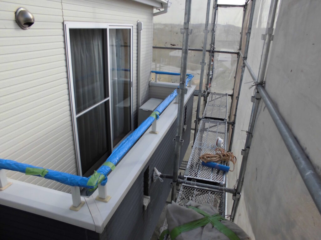 Scaffolding along a house exterior with a sliding glass door, blue-wrapped railing, and tools on the metal platform.