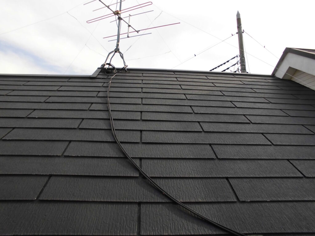 Black shingle roof with a mounted antenna on the ridge and a long black cable running down the surface.