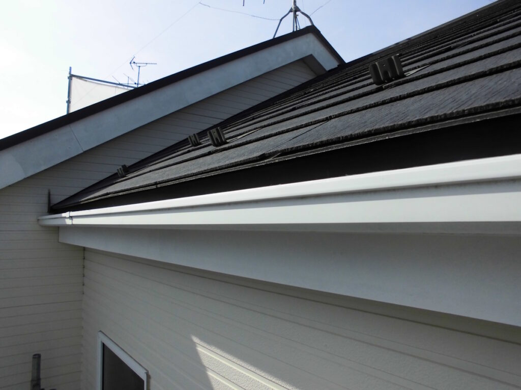 Close-up of a beige house showing a white gutter along the roof eave and a dark shingled roof.
