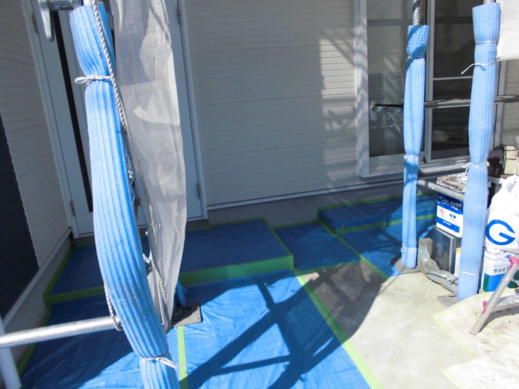 Scaffolding with blue padding around a doorway; blue ground tarps taped for protection outside a house.