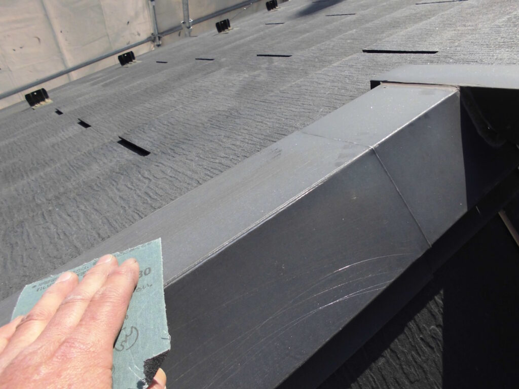 Close-up of a hand with sandpaper rubbing a gray metal roof edge during maintenance on a rooftop surface