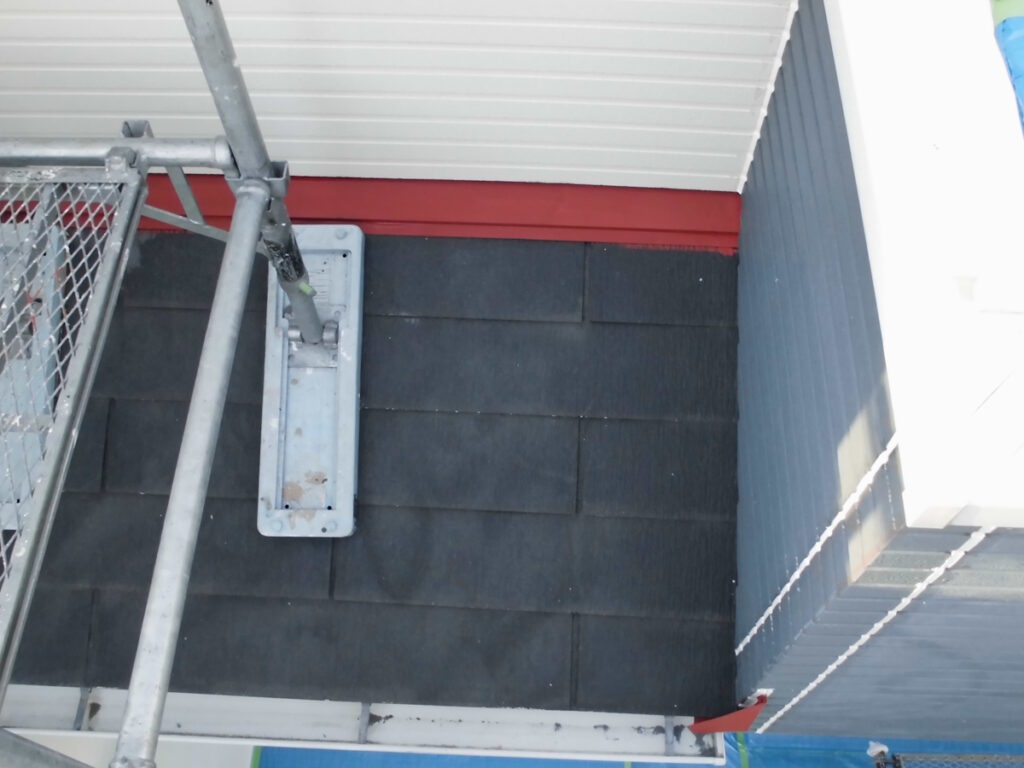 Metal scaffolding pole and base mounted on a dark shingled roof near red trim and blue siding.