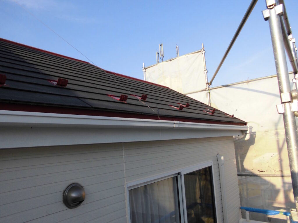 Side view of a house with a dark tile roof and scaffolding against a blue sky