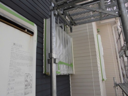 Scaffolding beside a dark siding house during renovation; a white vented utility panel is wrapped for protection.