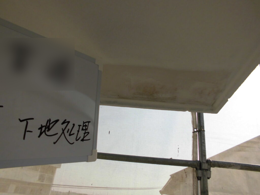 Sign on construction scaffold with handwritten Japanese text '下地処理' (surface preparation).