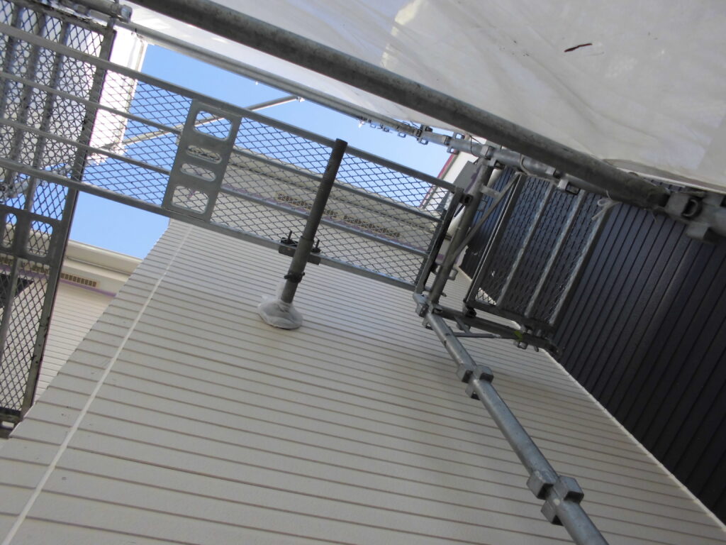 Exterior metal scaffolding and guardrails along a beige corrugated building, viewed from a tilted perspective with blue sky above