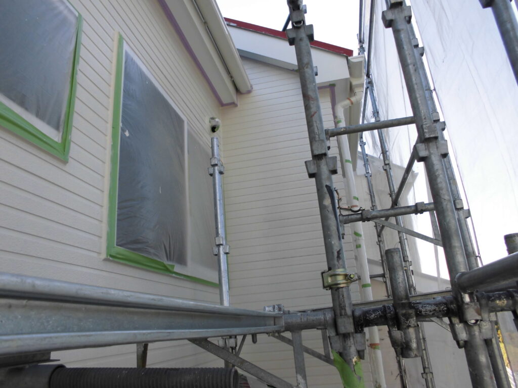 Exterior of a house under renovation with scaffolding and taped plastic-covered windows.