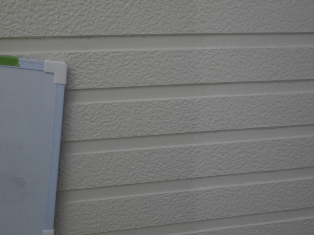 Whiteboard with green tape resting against textured horizontal siding on a building exterior.