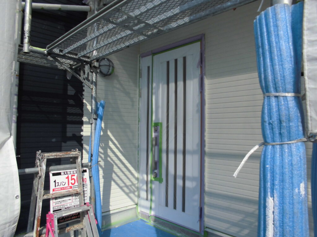 Under-construction doorway with a white door framed in green tape, surrounded by scaffolding and blue protective coverings.