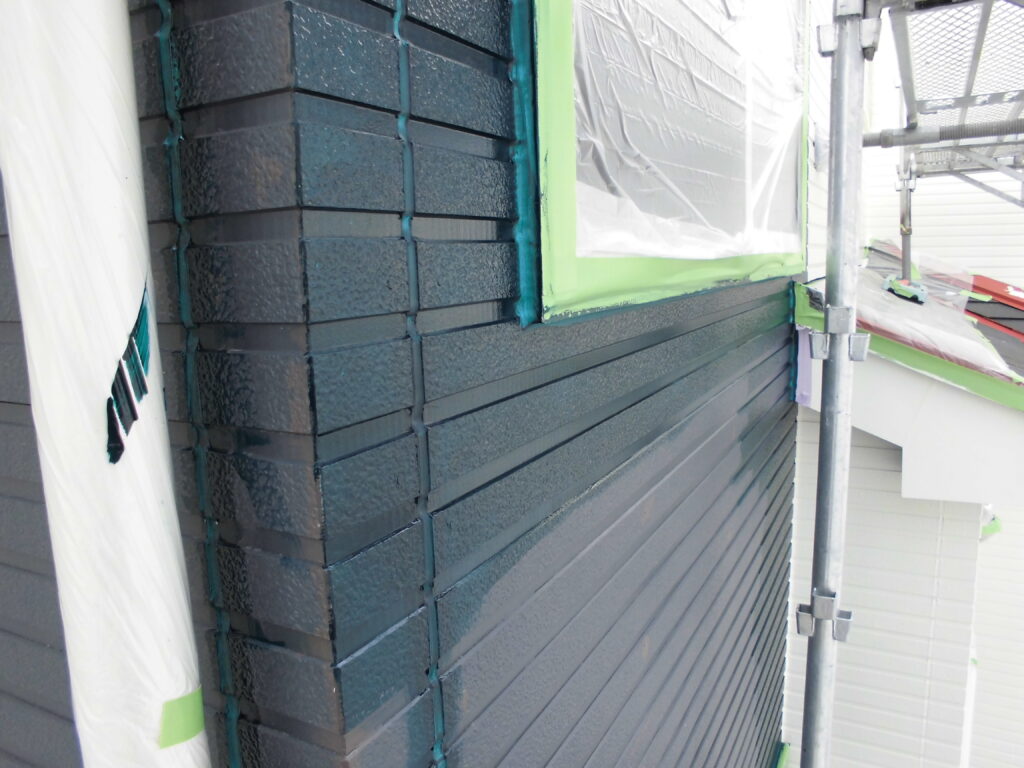 Exterior wall with dark blue horizontal siding being installed, scaffolding on the side and plastic-covered window nearby.