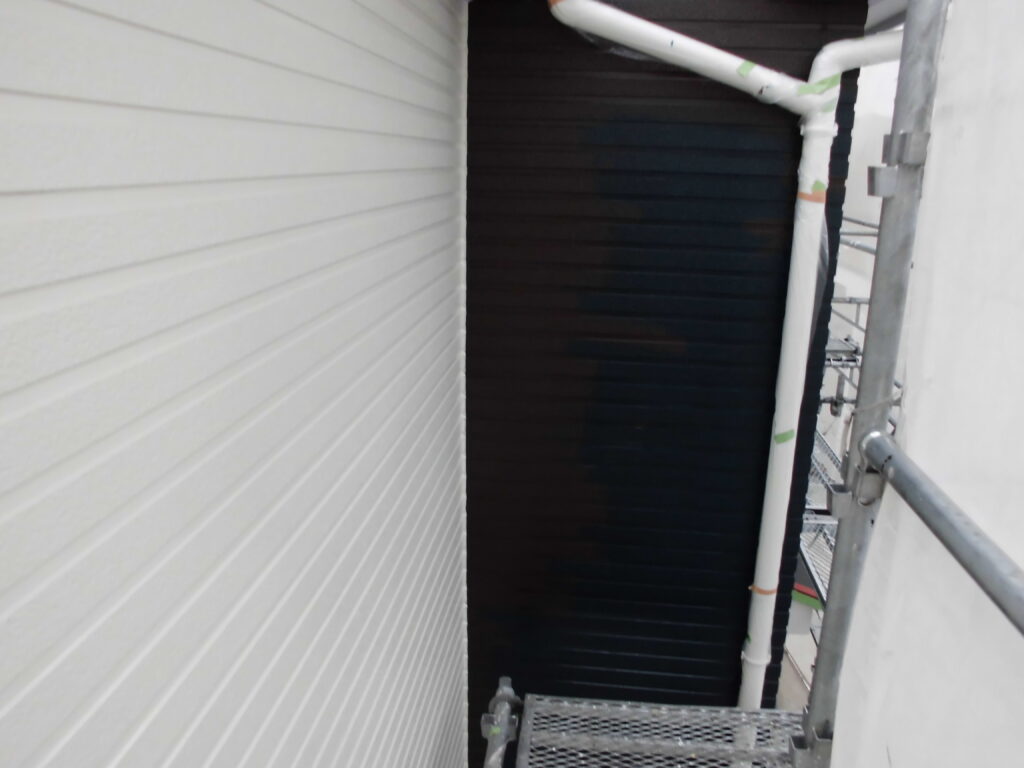 Narrow alley between white siding wall and dark vertical wall, with scaffolding and pipes against the right side.