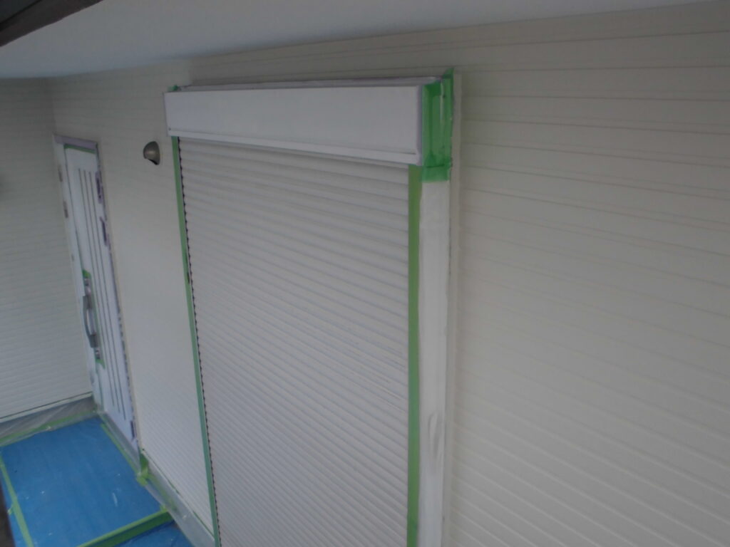 Exterior wall with white rolling shutter window masked with green painter's tape during renovation.