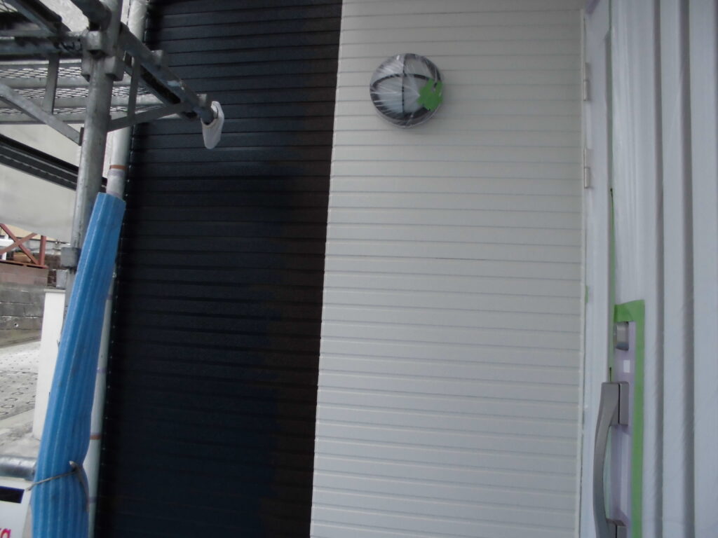 Exterior wall with white vertical siding and a black vertical stripe, scaffolding on the left, blue protective wrap, and a round vent with a green leaf sticker nearby.