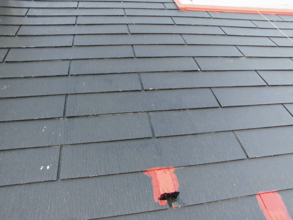 Dark gray shingled roof with a few red repair patches and a small hole in one section, indicating roof damage or maintenance.